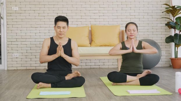 Happy Asian beautiful lifestyle family couple doing YOGA sitting meditating on lotus pose workout at home together on mat with eyes closed. Two people sport healthy concept.