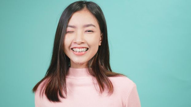 Portrait young Asian happy beautiful woman smiling wear silicone orthodontic retainers on teeth showing teeth model on hand isolated on blue background. dental hygiene and health concept