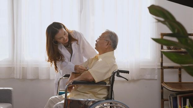 Female nurse doctor wear white uniform cardiologist examining patient senior or elderly old man during sit on wheelchair listening checking heartbeat using stethoscope at home, Health visitor concept