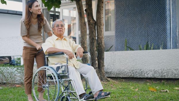 Disabled senior man on wheelchair with daughter, Happy Asian generation family having fun together outdoors backyard, Care helper young woman walking an elderly man smiling and laughed