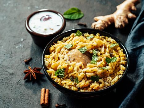Pakistani food - biryani rice with chicken and raita yoghurt dip. Delicious hyberabadi chicken biryani on black background