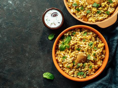 Pakistani food - biryani rice with chicken and raita yoghurt dip. Delicious hyberabadi chicken biryani in two bowl over black background. Top view or flat lay. Copy space