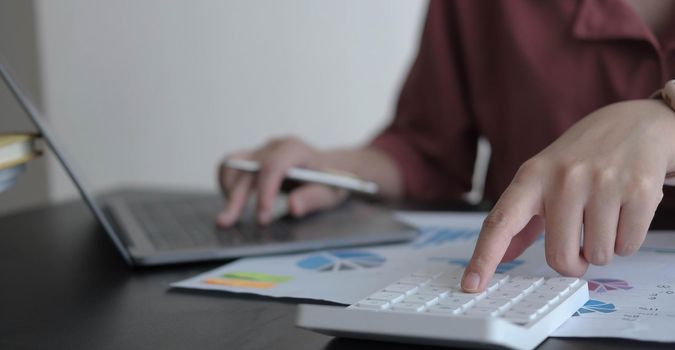 Close up Business woman using calculator and laptop for do math finance on wooden desk in office and business working background, tax, accounting, statistics and analytic research concept.