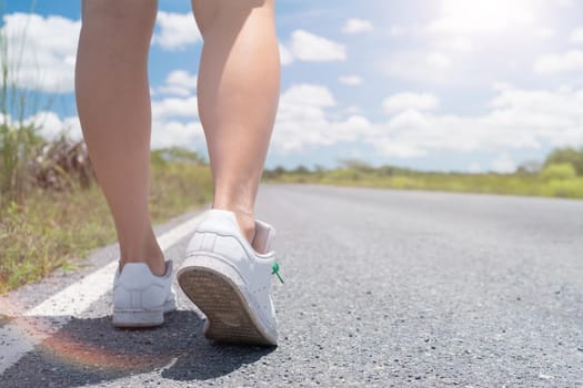 Woman is walking on small country road street with blue sky background.