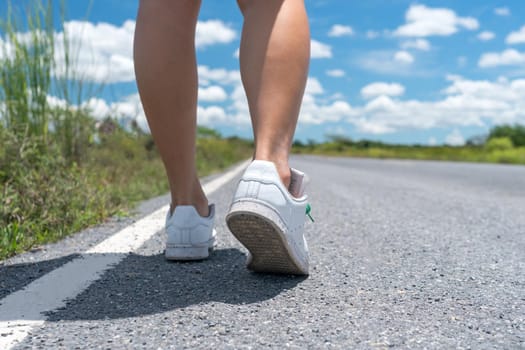 Woman is walking on small country road street with blue sky background.