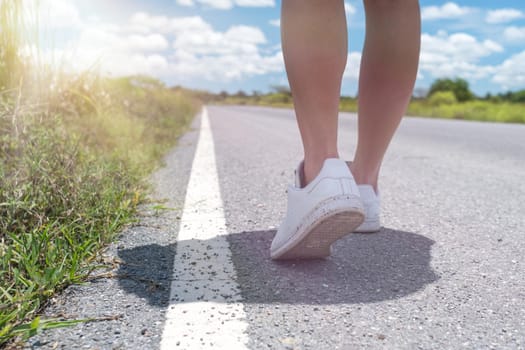 Woman is walking on small country road street with blue sky background.