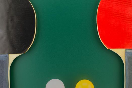 Red and black table tennis racks with a white and an yellow ping pong ball on green background with free copy space