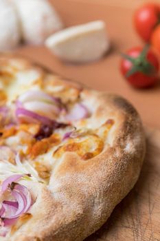 Pizza with cheese on a rustic wooden table. In the background out of focus cherry tomatoes and mozzarella.