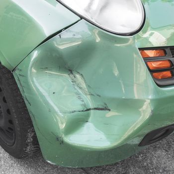 Green dented car. Side body of car was damaged by accident in traffic. Close-up.