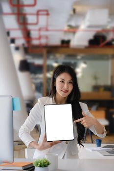 Business woman holding and pointing at digital tablet with blank screen in coffee shop