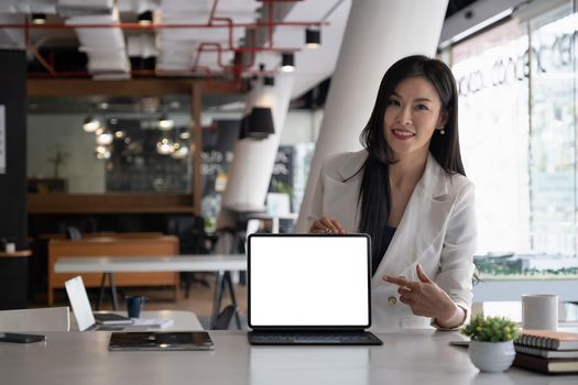 Business woman holding and pointing at digital tablet with blank screen in coffee shop.