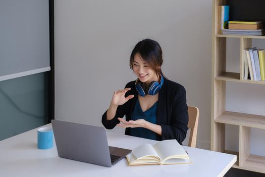 Happy young asian business woman with headphone to greeting or presentation to partner during making video conference with her team