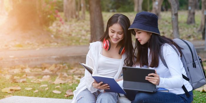 Two students are sitting in park during reading a book and communication. Study, education, university, college, graduate concept