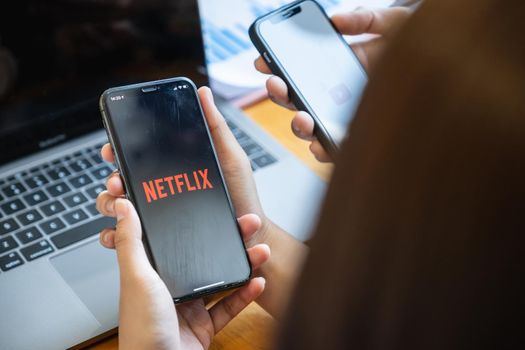 CHIANG MAI, THAILAND - FEB 11, 2021 : Woman and friend holding Phone with Netflix logotype on a screen and sharing her movie list