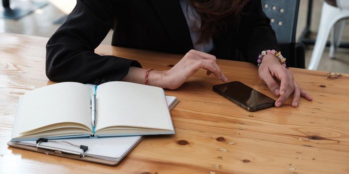 Closeup of business woman hand using mobile smart phone and reading message via application. Woman with a finger on the screen using a mobile phone in the office