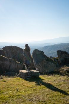 Caucasian young woman with brown dog on top of a boulder stone seeing Sortelha nature mountain landscape, in Portugal