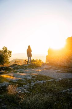 Caucasian young woman with brown dog seeing Sortelha nature mountain landscape with sun flare on a boulder, in Portugal