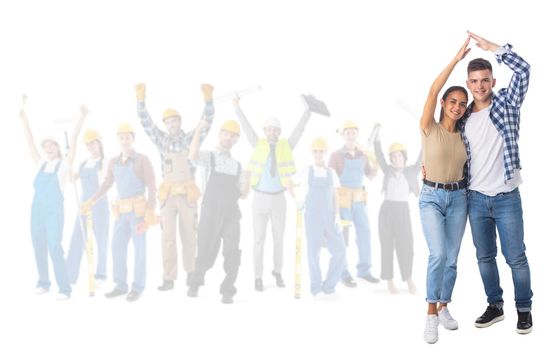 Happy young couple holding hand over the head showing house roof sign and happy construction workers on background isolated on white background