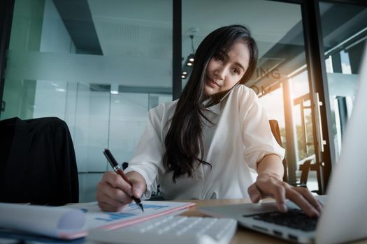 Business woman hand holding pen and pointing at financial paperwork with financial network diagram