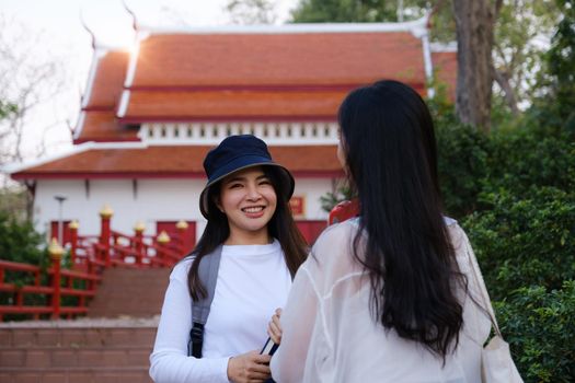 Asian woman traveler with backpack using maps on tablet and sitting in park, travel holiday relaxation concept.