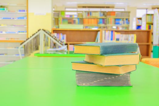 old book and heap treatise in school library on table green. blurry bookshelves background. education learning concept with copy space add text