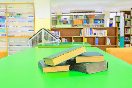 old book and heap treatise in school library on table green. blurry bookshelves background. education learning concept with copy space add text