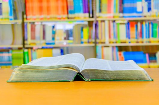 old book open in school library on wooden table. blurry bookshelves background. education learning concept with copy space add text