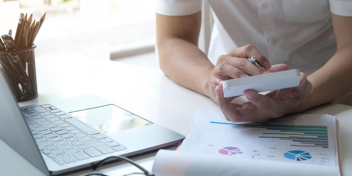 Close up Businessman using calculator and laptop for do math finance on wooden desk in office and business working background, tax, accounting, statistics and analytic research concept.