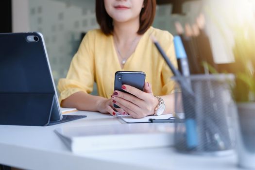 Young asian business woman using smart phone for contact customer on wooden desk in office. Business portrait concept