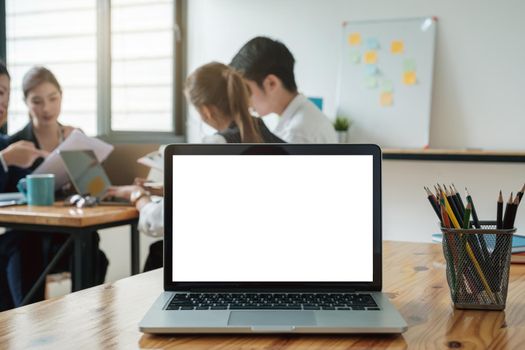 Laptop computer mockup and blank screen on wooden table with business team working background and morning light