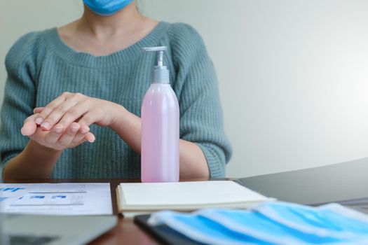 Businesswoman in mask washing hands by alcohol sanitizers or alcohol gel from pump bottle to kill corona virus or covid-19. work from home concept