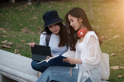 Two students are sitting in park during reading a book and communication. Study, education, university, college, graduate concept