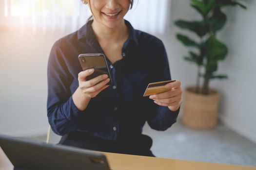 Woman in casual shirt paying with credit card online while making orders via application on cell phone. Successful and happy business woman making transaction using mobile bank application