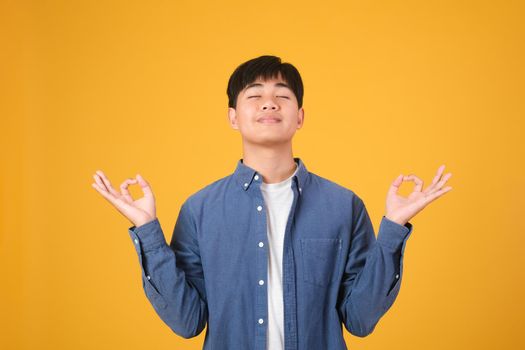 Stress management concept. Peaceful young man meditating, finding inner balance and harmony on yellow orange studio background.