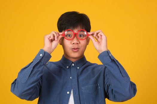 Portrait of asian nerd man with red glasses on yellow background, studio shot.