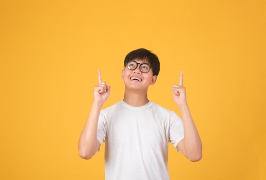 Happy smiling young asian man with amazed and surprised looking up and pointing to empty space above. 