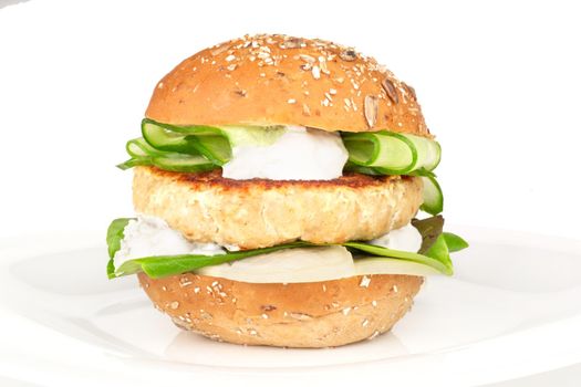 Fishburger fish burger with cod cutlet cucumber lettuce goat cheese dzatziki tartarus sauce and grain cereal bread on plate isolated on white background