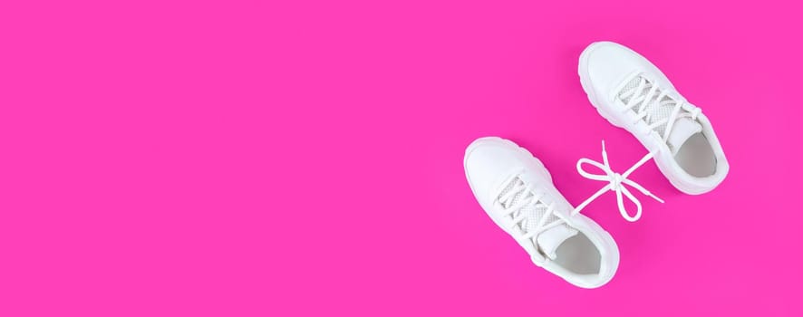 Pair of white sport shoes connected with laces bow on pink background. Simple flatlay with copy space.