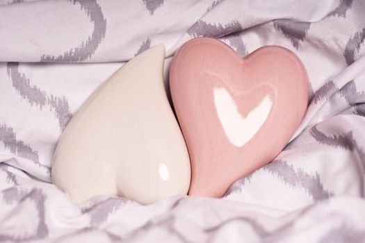 Heart shaped ceramic decorations fitting into each other on a modern pillow or bedsheet. Two red hearts on a bed. Valentine's Day and Wedding Day concept.