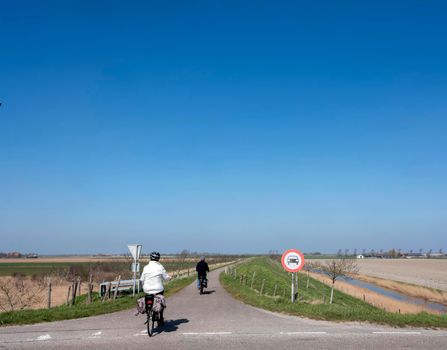 people ride bicycle on sunny spring day in dutch countryside of zeeland under blue sky