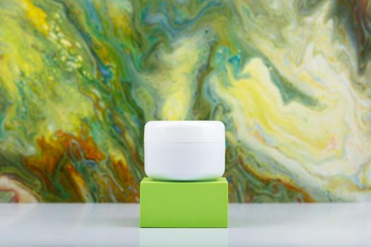 White cosmetic jar on green podium against green marbled background with copy space. Concept of beauty products for every day skin care and fresh, young looking skin