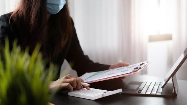 businesswoman wearing protective mask using calculator and calculating financial report in office.