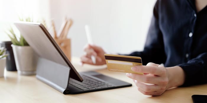 Close up hand of woman holding credit card and using laptop computer at home. Online shopping concept.