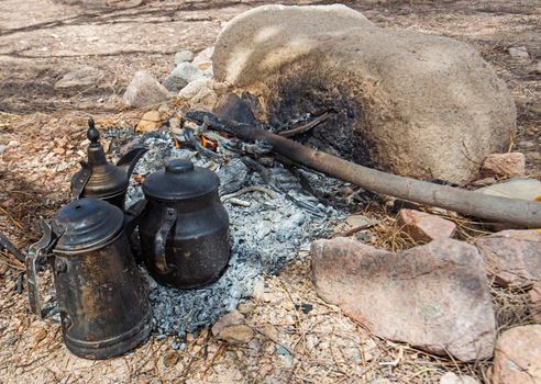 Landscape scenic view of campfire burning with cooking pots in barren desert environment