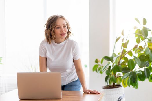 Business woman using laptop standing near desk white office interior with houseplant looking a side Business people Business person Online, Young and successful Dresed white shirt and jeans