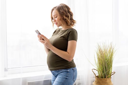 Pregnant woman use smartphone standing near big window Pregnancy Caucasian female with cell phone Modern technology concept