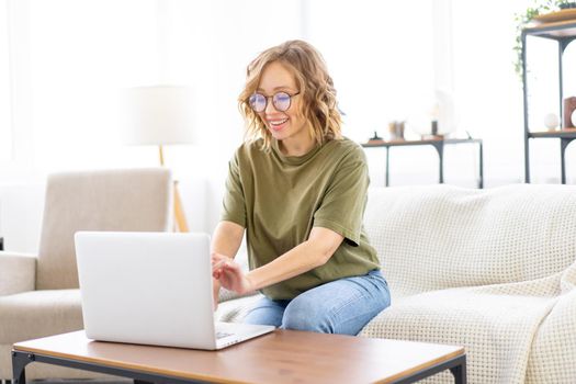 Woman with glasses use laptop typing keyboard sitting couch big window background home interior Freelance female working from home Distance learning student relaxing watch lessons video conference.