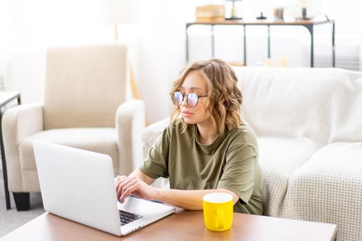 Woman with glasses use laptop drink morning coffee sitting floor near sofa big window background home interior Freelance female working home Distance learning student relaxing watch video lessons.