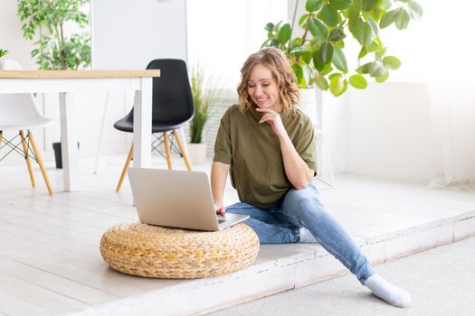 Woman using laptop computer while sitting floor at home interior. Freelance female working from home Distance learning student relaxing and watch lessons on video conference .