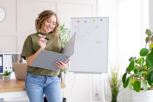 Businesswoman holding folder for paper write marker thinking dreaming standing near office table. Business person femal ypoung adult caucasian on modern white interior